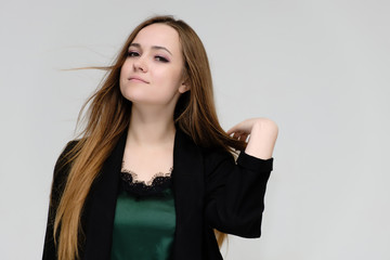 Fototapeta premium Concept close-up portrait of a pretty girl, a young woman with long beautiful brown hair and a black jacket on a white background. In the studio in different poses showing emotions.