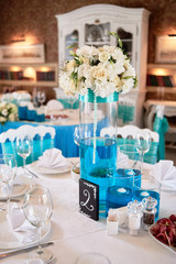 Beautiful floral arrangement and candles in glass vases on wedding table in restaurant, copy space. Luxury wedding decorations. Table setting