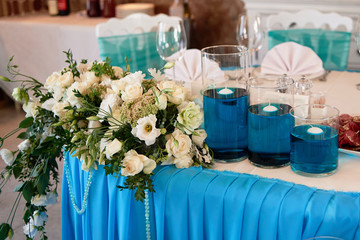 Lush floral arrangement and candles in glass vases on wedding presidium in restaurant, copy space. Banquet table for newlyweds. Luxury wedding decorations
