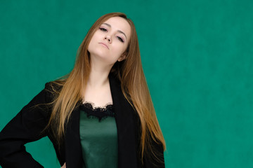 Concept close-up portrait of a pretty girl, a young woman with long beautiful brown hair and in a black jacket on a green background. In the studio in different poses showing emotions.