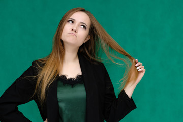 Concept close-up portrait of a pretty girl, a young woman with long beautiful brown hair and in a black jacket on a green background. In the studio in different poses showing emotions.