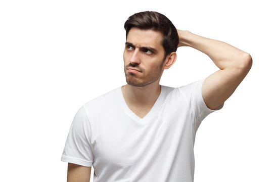 Young doubtful man scratching his head trying to find solution, isolated on gray background
