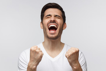 Soccer fan concept. Young attractive man shouting while his team win, raised both fists in victory gesture, isolated on gray background