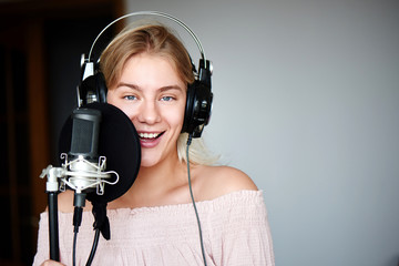 Beautiful blonde singer girl in headphones in home recording studio sings a song into a microphone,...