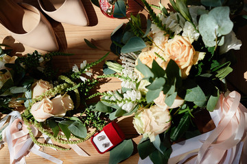 Bridal bouquet of roses and greenery, boutonniere, earings and beige bride's shoes on wood floor background, copy space. Wedding concept. Top view, flat lay. Bridal accessories