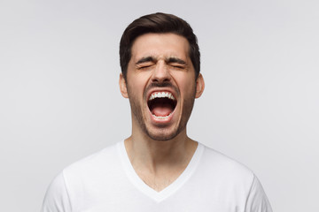 Angry man, rage concept. Close-up portrait of screaming with closed eyes crazy young man isolated,...