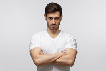 Fototapeta premium Young man in standing with arms crossed and serious concentrated face at camera, looking aggressive, isolated on gray background