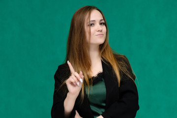 Concept close-up portrait of a pretty girl, a young woman with long beautiful brown hair and in a black jacket on a green background. In the studio in different poses showing emotions.