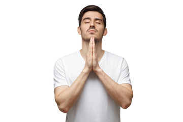 Young man putting hands together as if he is praying with closed eyes, isolated on white background