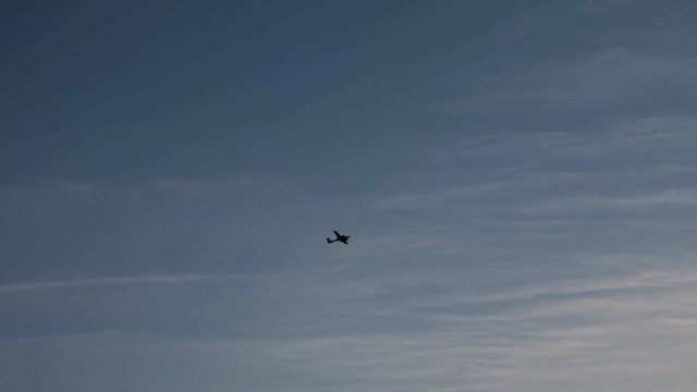 Silhouette of airplane flying in sunset sky. Plane is gaining altitude after take off at the airport. Passenger jen among clouds. Spotting concept.