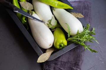 White eggplants, bitter pepper, garlic, bay leaf, green arugula on a protvine, which stands on a...