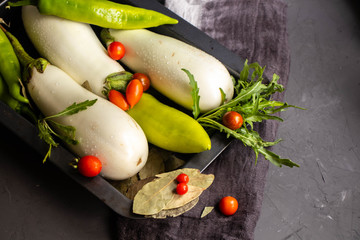 White eggplants, bitter pepper, garlic, bay leaf, green arugula on a protvine, which stands on a gray background. 