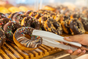 Human hand using clamp picking chocolate donut at pastry shop