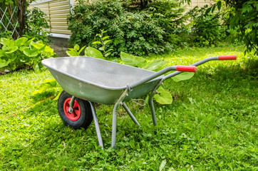 garden trolley with red handles and wheels stands on the grass
