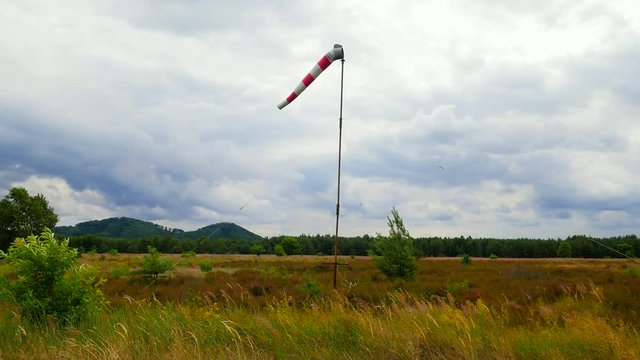 Windsock blown by the wind with overcast sky, lonely tree and green lawn. Abandoned windsock in wind 