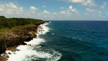 Waves of the blue ocean crashing against the shore and rocks against the sky with clouds. Siargao, Philippines. Summer and travel vacation concept