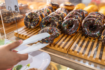 Hand holding clamp picking frosted chocolate donut at pastry shop