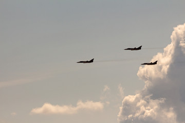 silhouettes of three military aircraft on the background of clouds and blue sky