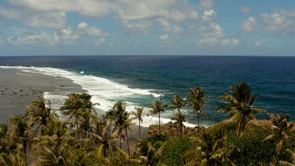 Travel concept: Coast of a tropical island with palm trees and ocean waves rolling on the beach. Siargao, Philippines.