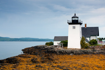 Fototapeta na wymiar Sun Breaks Through Clouds Illuminates Maine Lighthouse at Low Tide in Maine