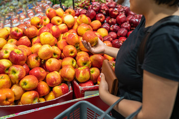 Asian woman picking apple at fruit stand in supermarket