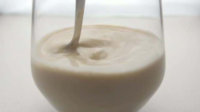 Coffee in glass mixing with metallic spoon. White background. Slow motion. Close-up.