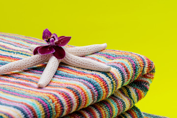 Folded Colorful Striped Organic Cotton Beach Towels decorated with White Finger Starfish and Orchid Flower on bright yellow background.