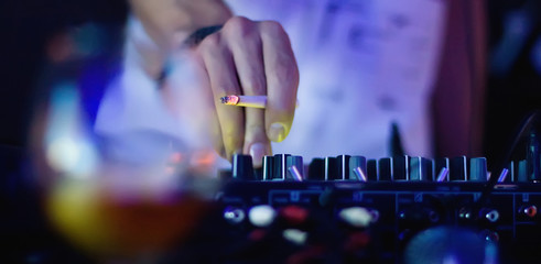 DJ hand holding a cigarette at the remote