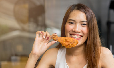 close up young pretty asian woman smiling and holding fried chicken (leg) for eating on brunch meal...