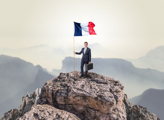 Obraz premium Successful businessman on the top of a mountain holding France victory flag