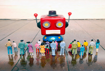 red robot head talks to a crowed of plastic people o