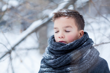 Portrait of sad boy in black coat for walk in winter park, outdoor