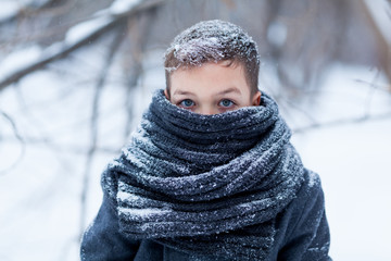 Portrait of sad boy in black coat for walk in winter park, outdoor