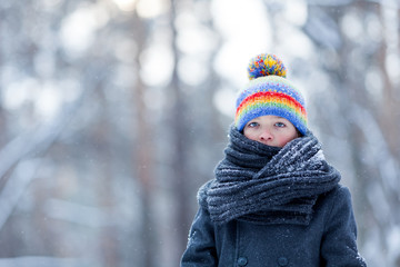 Portrait of sad boy in black coat for walk in winter park, outdoor