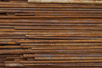 Top view stack of straight old rusty high yield stress deformed reinforcement steel or iron bars. Background horizontal random pattern of deformed iron bars. 