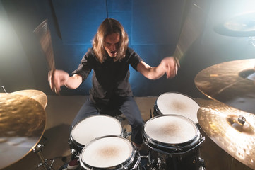 Portrait of a long-haired drummer with chopsticks in his hands sitting behind a drum set. Low key. Concepts of the creative freedom of the millenial generation