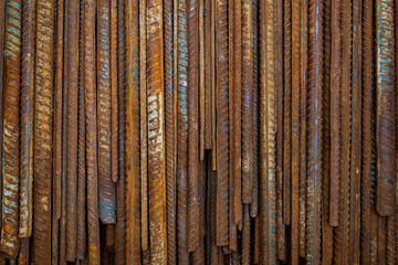 Fototapeta premium Top view stack of straight old rusty high yield stress deformed reinforcement steel or iron bars. Background vertical random pattern of deformed iron bars. 