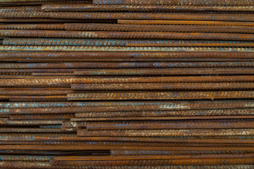 Top view stack of straight old rusty high yield stress deformed reinforcement steel or iron bars. Background horizontal random pattern of deformed iron bars. 