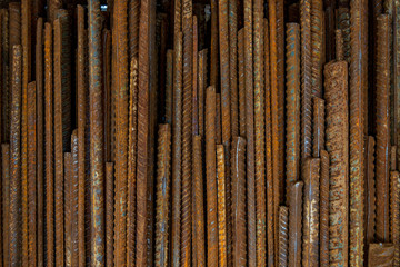 Top view stack of straight old rusty high yield stress deformed reinforcement steel or iron bars. Background vertical random pattern of deformed iron bars. 