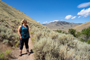 Blonde female hiker (30s) looks off into the distance while on a mountain hike. Taken in the Salmon-Challis National Forest of Idaho on Goldbug Hot Springs trail