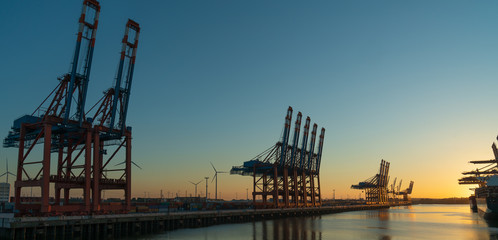 Obraz premium cranes in the hamburg harbour in the sunset