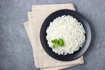 Steamed rice on black plate. Gray stone background. Top view.