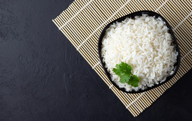 Steamed rice on black plate over bamboo tablecloth. Black stone background. Top view with copy...
