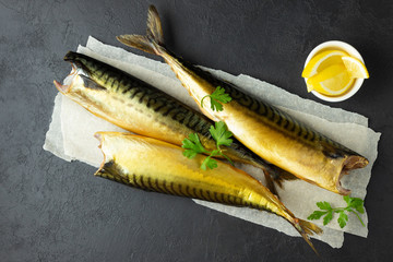 Smoked fish mackerel or scomber on a white parchment paper. Black or dark stone background. Top...