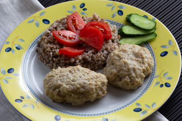Cooked buckwheat and meatballs on the plate decorated by tomato and cucumber