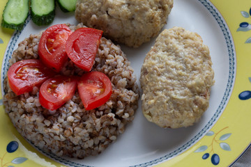 Cooked buckwheat and meatballs on the plate decorated by tomato and cucumber