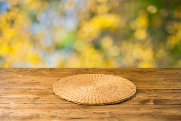 Empty wooden table with wicker round placemat over autumn nature park background