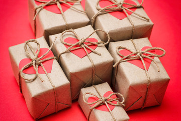 Set of brown gift boxes. Wrapped in craft paper and tied by hemp cord. Bright red background and carton hearts decorative card. 