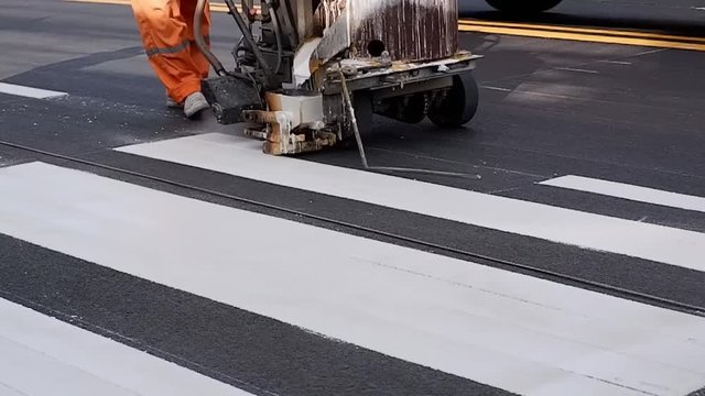 Slow motion: Low section of road worker using thermoplastic spray road marking machine to painting pedestrian crosswalk on asphalt road surface in the city
