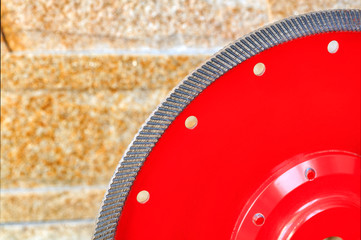 Fragment of a red diamond blade for cutting granite and stone against a background of a wall of golden sandstone.